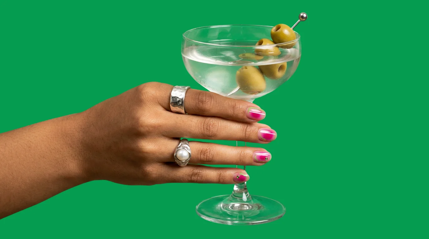 Martini with olives, held in front of a green backdrop — drinks from the 1000 Boxes lounge